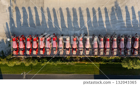 A fleet of tanker trucks is parked in a row, casting long shadows on the ground 132043365