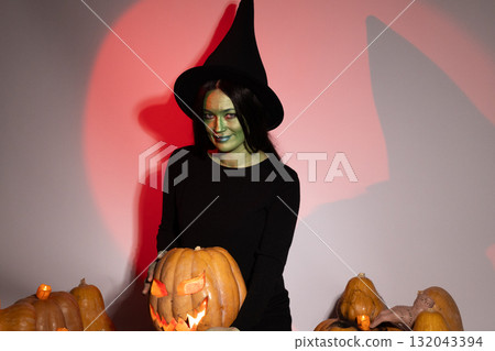 Woman in black dress and witch hat surrounded by glowing pumpkins. Woman in black dress and witch hat surrounded by glowing pumpkins. 132043394