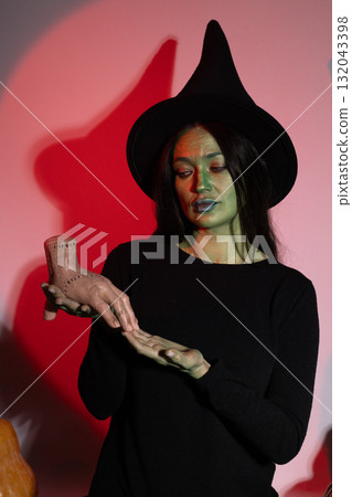 The witch in the image is holding a magical item, possibly casting a spell The witch in the image is holding a magical item, possibly casting a spell 132043398