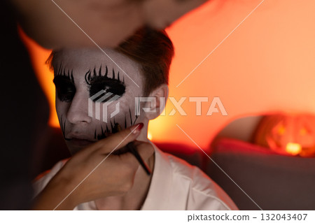 A person is applying Halloween-themed makeup to another person's face 132043407