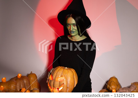 Woman in black shirt and witch hat holding pumpkin 132043425