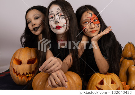 girls with face paint carving pumpkins, surrounded by autumn leaves and smiling  132043433