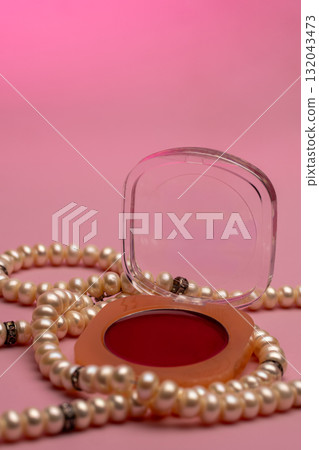 A strand of pearls and a round red jewelry box with a clear lid are resting A strand of pearls and a round red jewelry box with a clear lid are resting 132043473
