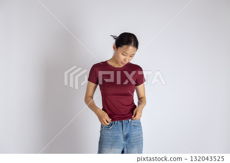 The woman is looking down and holding the waistband of her jeans with both hands The woman is looking down and holding the waistband of her jeans with both hands 132043525