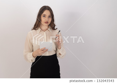 The woman is holding a pen and a small notebook while standing in front  132043543
