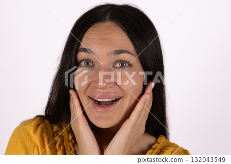 The woman is holding her face with her hands and smiling, appearing surprised  132043549
