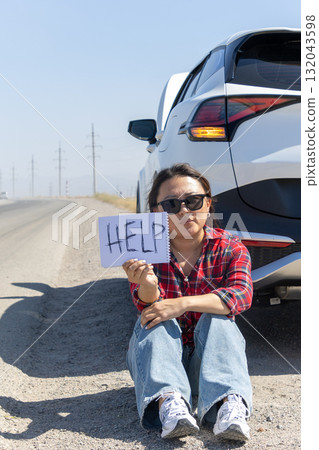 Woman sitting on road holding help sign 132043598