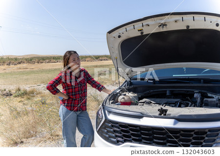 Woman standing next to open car hood, examining engine 132043603