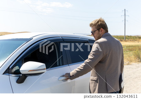 A man is reaching to open the door of a white car 132043611