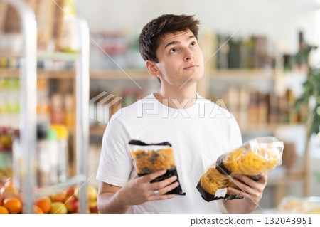 Guy chooses tasty italian pasta to buy in grocery department section of store Guy chooses tasty italian pasta to buy in grocery department section of store 132043951