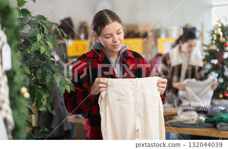 Glad young girl choosing pantaloons in clothing store Glad young girl choosing pantaloons in clothing store 132044039