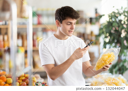 Checking expiration date of chips - guy shopper scans QR code on label of chips using smartphone 132044047