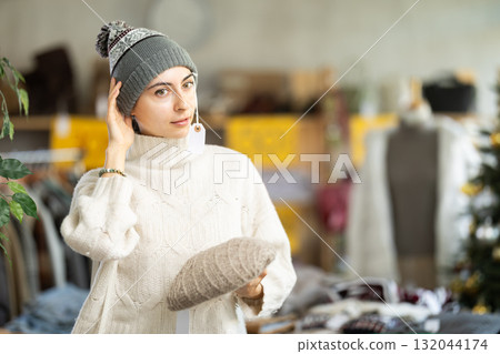 Young Armenian girl choosing hat in clothing store Young Armenian girl choosing hat in clothing store 132044174