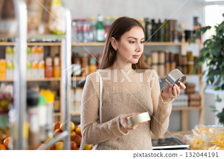Young woman holding two tin cans of preserves in hands, choosing and shop around pate for sandwiches 132044191