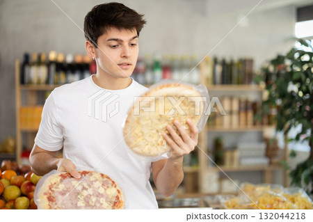 Thoughtful guy choosing frozen pizzas in grocery store Thoughtful guy choosing frozen pizzas in grocery store 132044218