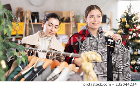 Two happy friends choosing coat or jacket in clothing store 132044234