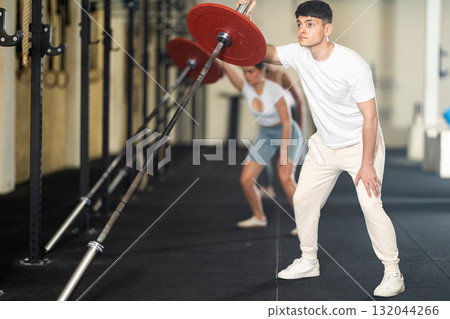 Athletic young guy pumping up her arm biceps using one side of barbell 132044266