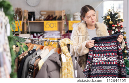 Uncertain young girl choosing sweater in clothing store Uncertain young girl choosing sweater in clothing store 132044305