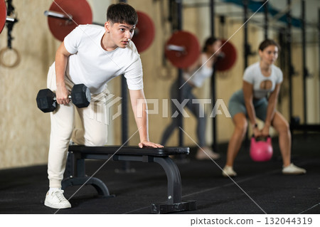 Young guy training with dumbbells on bench 132044319