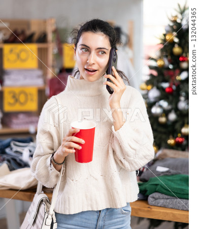 Armenian girl with cup of coffee talking on phone in womens clothing store Armenian girl with cup of coffee talking on phone in womens clothing store 132044365