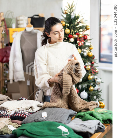Uncertain young Armenian girl choosing sweater in clothing store 132044380