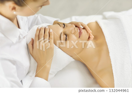 Close up photo of pretty young woman lying with closed eyes and having face or head massage in spa Close up photo of pretty young woman lying with closed eyes and having face or head massage in spa 132044961