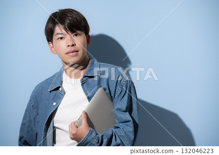 A young man wearing denim and holding a laptop. Image of an engineer, designer, or freelancer. A young man wearing denim and holding a laptop. Image of an engineer, designer, or freelancer. 132046223