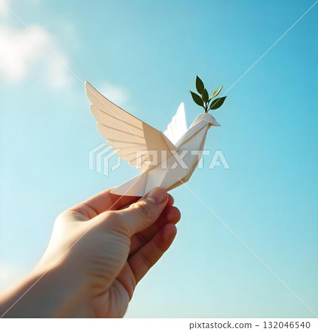 Person holds a paper origami bird aloft, symbolizing peace and hope against a serene natural background 132046540