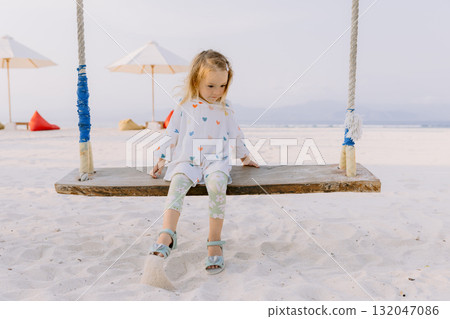 Little child girl on swings on tropical beach, enjoy childhood 132047086