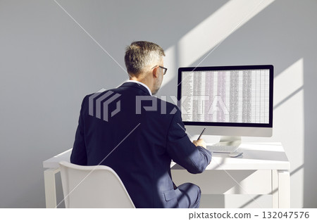 Businessman or accountant at workplace compares data on electronic spreadsheet on computer. Businessman or accountant at workplace compares data on electronic spreadsheet on computer. 132047576