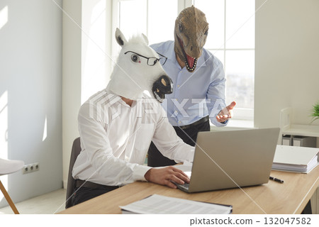 Two men in funny horse and dinosaur masks use notebook computer at work in office Two men in funny horse and dinosaur masks use notebook computer at work in office 132047582