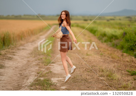 Woman joyfully spinning on a rural path surrounded by fields on a sunny day 132050828