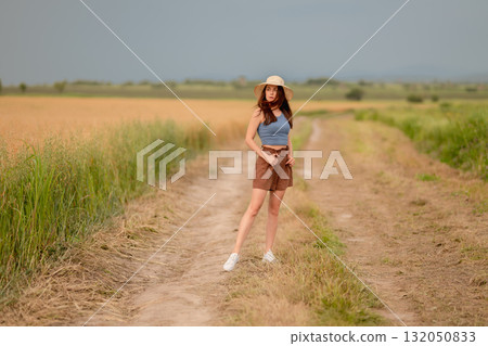 Young woman poses confidently in a grassy field under a cloudy sky during late afternoon Young woman poses confidently in a grassy field under a cloudy sky during late afternoon 132050833