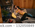 Couple sharing a cozy moment on a couch in a wooden cabin during a chilly evening 132050849