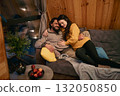 Couple enjoying a cozy evening together in a wooden cabin by the warmth of the sofa 132050850