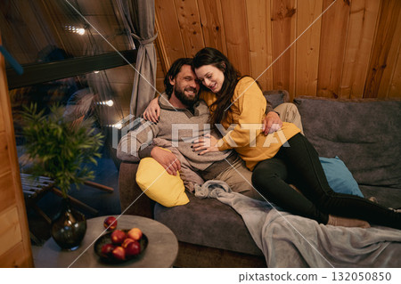 Couple enjoying a cozy evening together in a wooden cabin by the warmth of the sofa Couple enjoying a cozy evening together in a wooden cabin by the warmth of the sofa 132050850