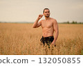 Man in a wheat field holds grains as he enjoys a peaceful moment during golden hour 132050855