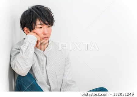 A young Asian man looking down and depressed while resting his chin on his hands A young Asian man looking down and depressed while resting his chin on his hands 132051249