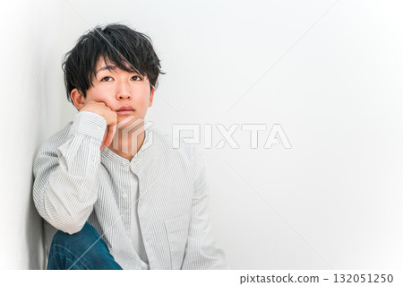 A young Asian man resting his chin on his hand and staring blankly into the distance A young Asian man resting his chin on his hand and staring blankly into the distance 132051250
