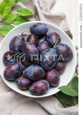 Fresh ripe plums in white bowl on table 132052023