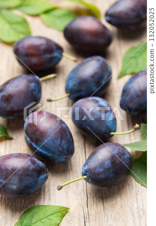 Ripe purple plums fallen on wooden table 132052025