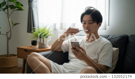 早安.坐在沙發上,一邊刷牙一邊看手機。 早安.坐在沙發上,一邊刷牙一邊看手機。 132052174