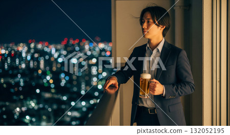 一名男子站在公寓大樓的陽台上，凝視著夜景。他手裡拿著一瓶啤酒，頭髮在夜風中飄揚。 132052195