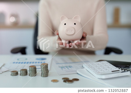 Financial savings. A person holding a piggy bank and reviewing financial documents. 132052887