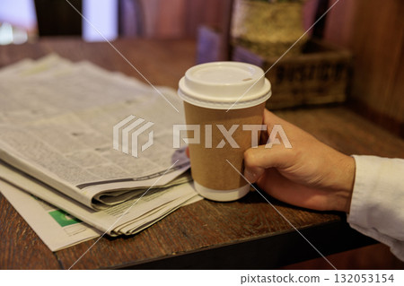 Hand holding coffee and English newspaper Hand holding coffee and English newspaper 132053154