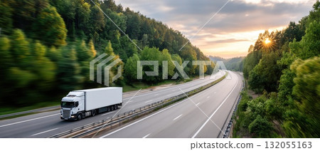 A truck drives swiftly on a winding road, framed by majestic mountains and vibrant greenery under a clear sky during daylight 132055163