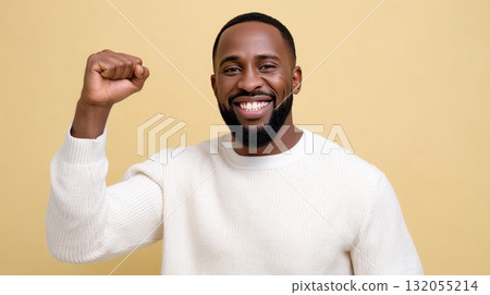 A cheerful man with a beard shows his excitement by raising his fist while smiling broadly against a soft background 132055214