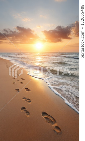Footprints lead across a sandy beach as the sun sets, creating a serene atmosphere with waves softly touching the shore 132055488