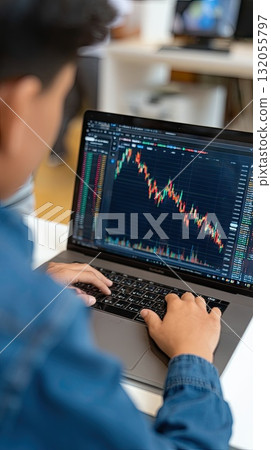 A focused individual types on a laptop, reviewing stock market data and trends on an open chart, highlighting financial analysis work 132055797
