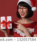 close up of woman in santa hat, glasses winking at a gift box 132057584